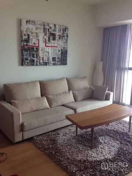 Condominium for rent in Sathon, Bangkok - Cozy lounge corner with beige sofa, shag rug, wooden coffee table, and wall art beside a full-height window.