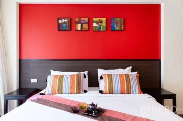 公寓 出租在Bang Rak, Bangkok - 特大床近景，条纹抱枕，红色背景墙与装饰画。