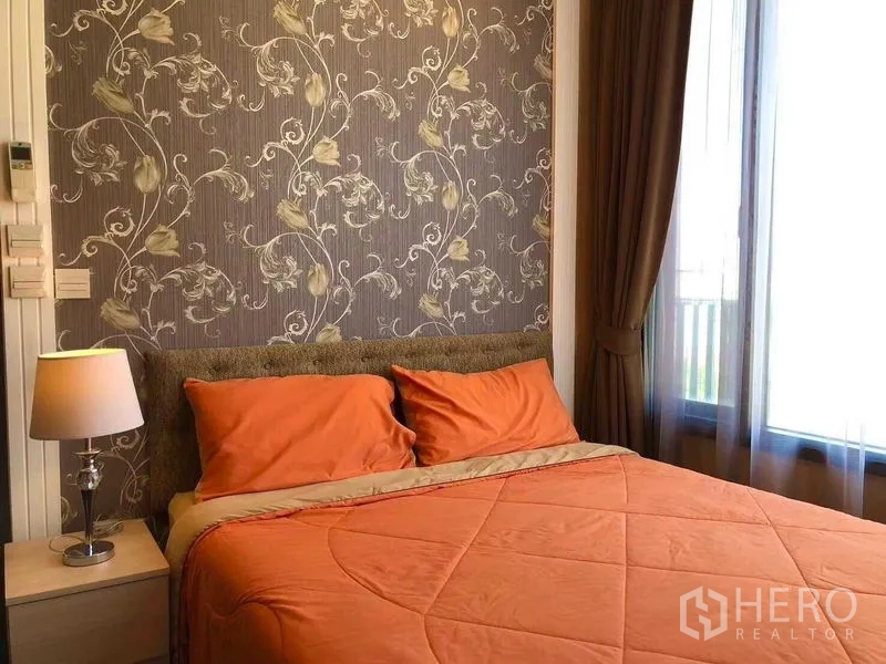 คอนโด ให้เช่าหรือขายในWatthana, Bangkok - ห้องนอนติดวอลเปเปอร์ลายดอกไม้ ชุดเครื่องนอนสีส้ม และโคมไฟหัวเตียง