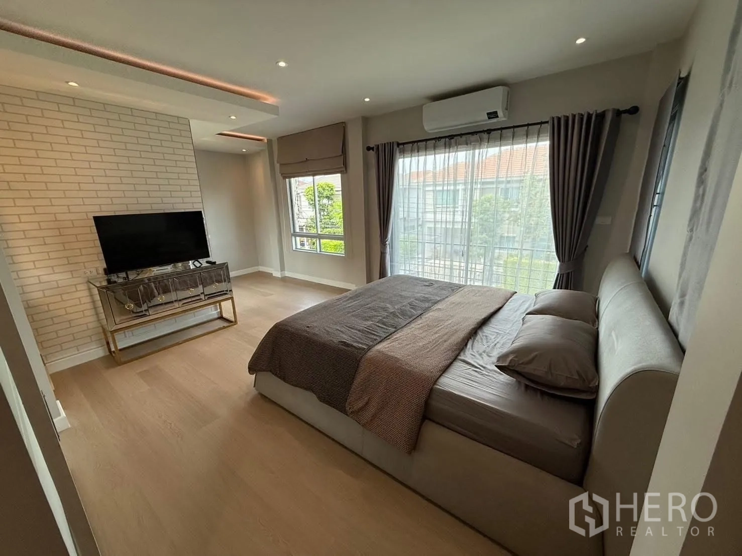 Detached House for rent in Prawet, Bangkok - Master bedroom with king bed, TV console, brick accent wall, full-height curtains and air conditioner.