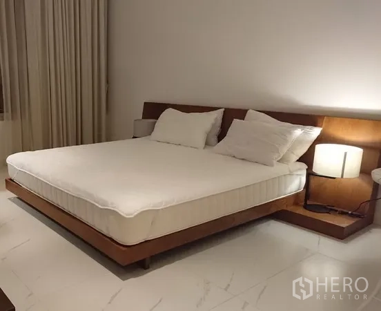 คอนโด ให้เช่าในPathum Wan, Bangkok - ห้องนอนกว้าง เตียงคิงส์ไซซ์แบบแพลตฟอร์ม หัวเตียงไม้ โคมไฟข้างเตียง และพื้นกระเบื้องใหญ่