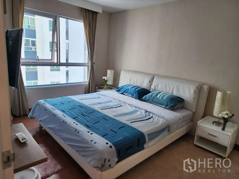 Condominium for rent in Huai Khwang, Bangkok - Master bedroom with large bed, bedside tables and wide window overlooking neighboring towers.