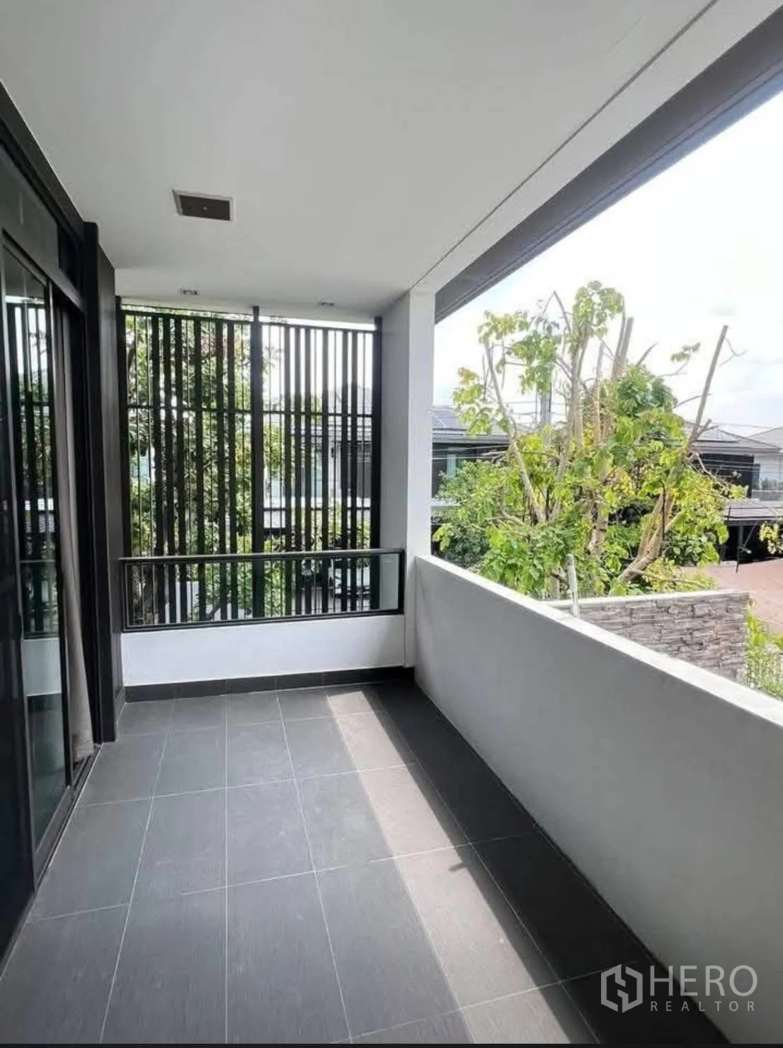 บ้านเดี่ยว for rent in Bang Phli, Samut Prakan - ระเบียงมีหลังคาปูพื้นกระเบื้องและฉากซี่เหล็กมองเห็นต้นไม้ด้านนอก
