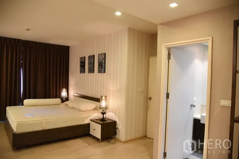 Condominium for rent in Khlong Toei, Bangkok - Master bedroom with king bed, bedside lamps, wood floors and a door leading to an ensuite bathroom.