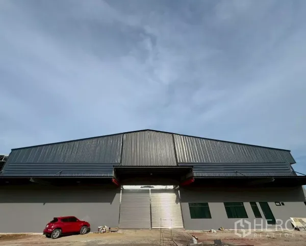 Warehouse for rent in Krathum Baen, Samut Sakhon - Front elevation of a newly built gray warehouse with wide roller shutter and loading canopy in Krathum Baen.