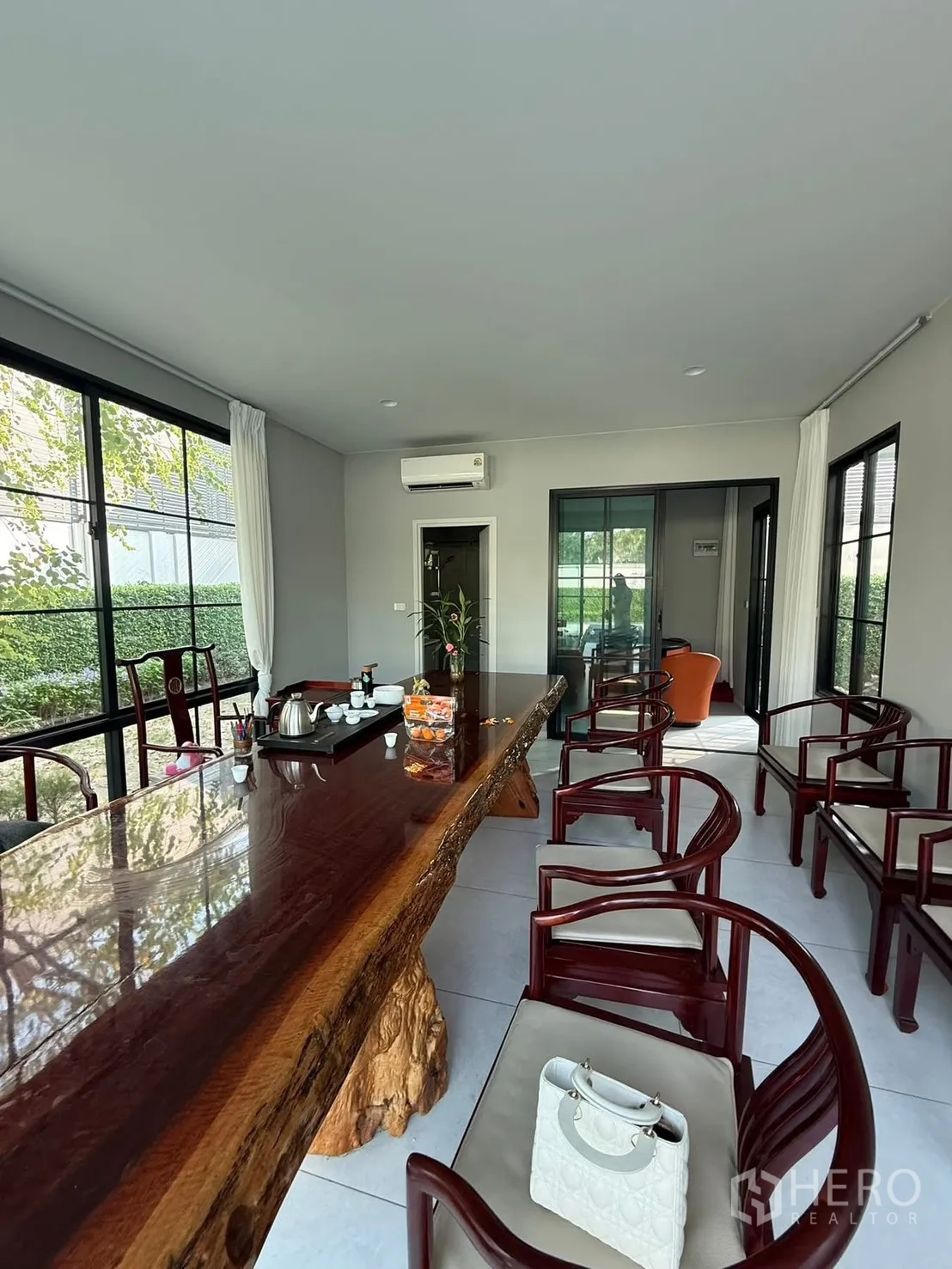 Detached House for rent in Bang Kapi, Bangkok - Glass-walled lounge with a long live-edge wooden table and classic chairs overlooking the garden.