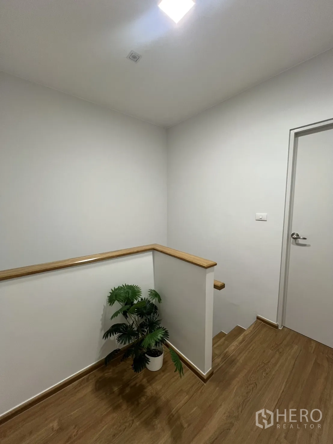 Townhouse for rent in Bang Phli, Samut Prakan - Stair landing with wood handrail and a potted plant on wood flooring.