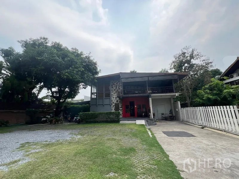 บ้าน ให้เช่าในKhlong Toei, Bangkok - มุมสนามหน้าบ้าน แสดงสนามหญ้ากว้าง ลานจอดรถโรยหิน และรั้วไม้สีขาวของบ้านเดี่ยว