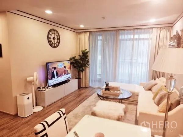 公寓 出售在Bang Rak, Bangkok - 明亮客厅，白色沙发、圆形玻璃茶几、电视柜、室内绿植与落地纱帘，木地板。