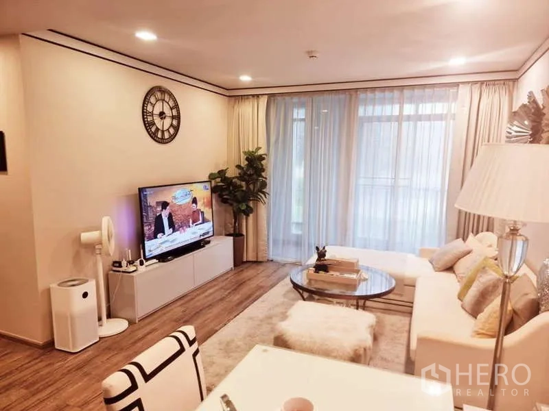 公寓 出售在Bang Rak, Bangkok - 明亮客厅，白色沙发、圆形玻璃茶几、电视柜、室内绿植与落地纱帘，木地板。