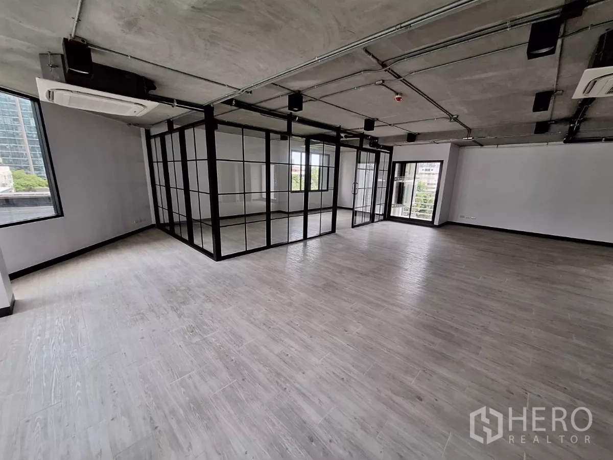 Office Space for rent in Watthana, Bangkok - Open-plan office with glass-walled meeting room, light wood flooring, exposed ceiling, and large windows.