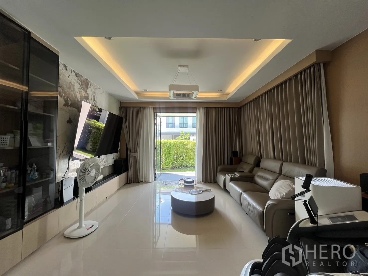 Detached House for rent or sale in Mueang Pathum Thani, Pathum Thani - Contemporary living room with large sofa, TV feature wall and sliding doors to the garden.