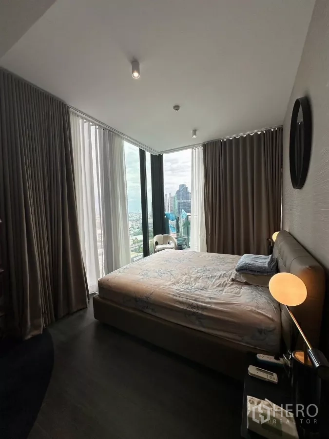 คอนโด ให้เช่าในBang Rak, Bangkok - ห้องนอนมุมกระจกเต็มบาน มีโคมไฟข้างเตียง และวิวเมืองกรุงเทพฯ กว้างไกล