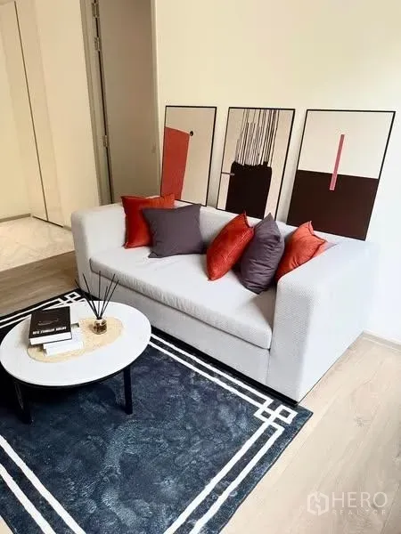 Condominium for rent - Modern living room with light gray sofa, colorful cushions, abstract art and a round coffee table on a dark rug.