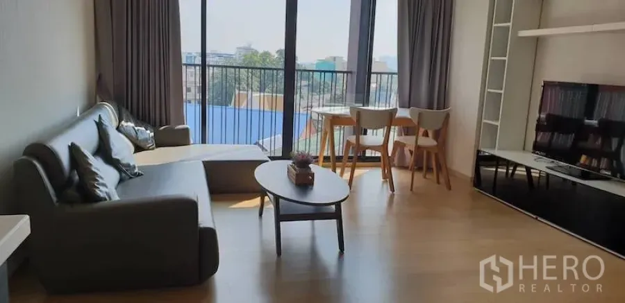 Condominium for rent in Watthana, Bangkok - Open-plan living and dining area with sofa, coffee table, TV cabinet and floor-to-ceiling windows overlooking the city.