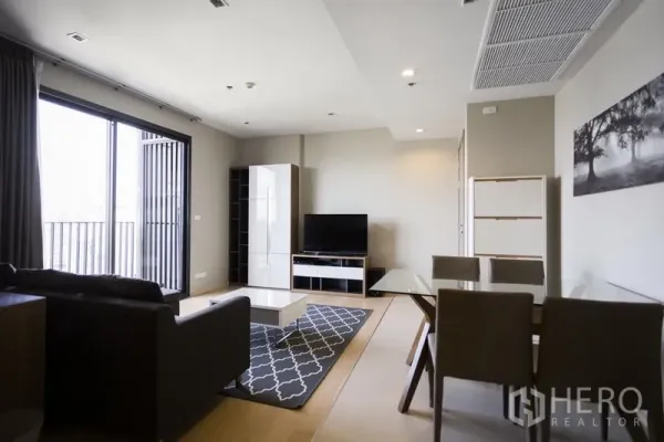 คอนโด ให้เช่าในWatthana, Bangkok - พื้นที่นั่งเล่นกว้างพร้อมชั้นวางทีวี ประตูกระจกออกระเบียง และมุมรับประทานอาหารโทนเรียบ