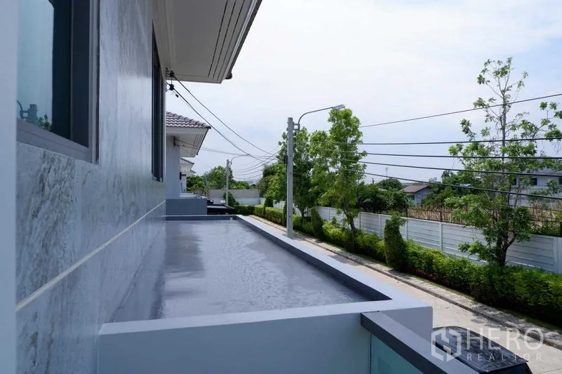 บ้าน ขายในLat Krabang, Bangkok - ระเบียงยาวมองเห็นถนนเงียบสงบมีต้นไม้เรียงราย