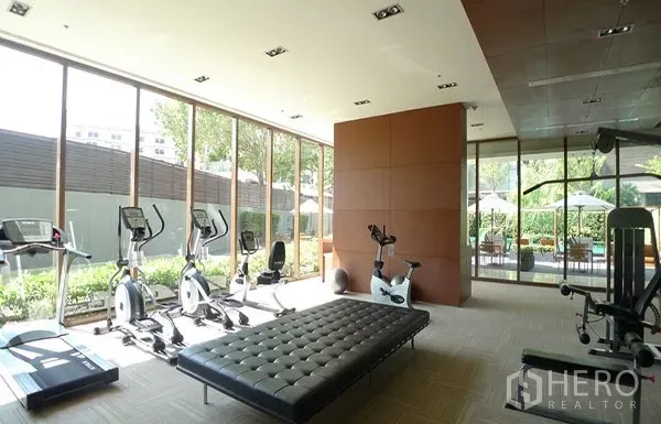 Condominium for rent or sale in Khlong Toei, Bangkok - Glass-walled fitness room with cardio machines facing garden views.