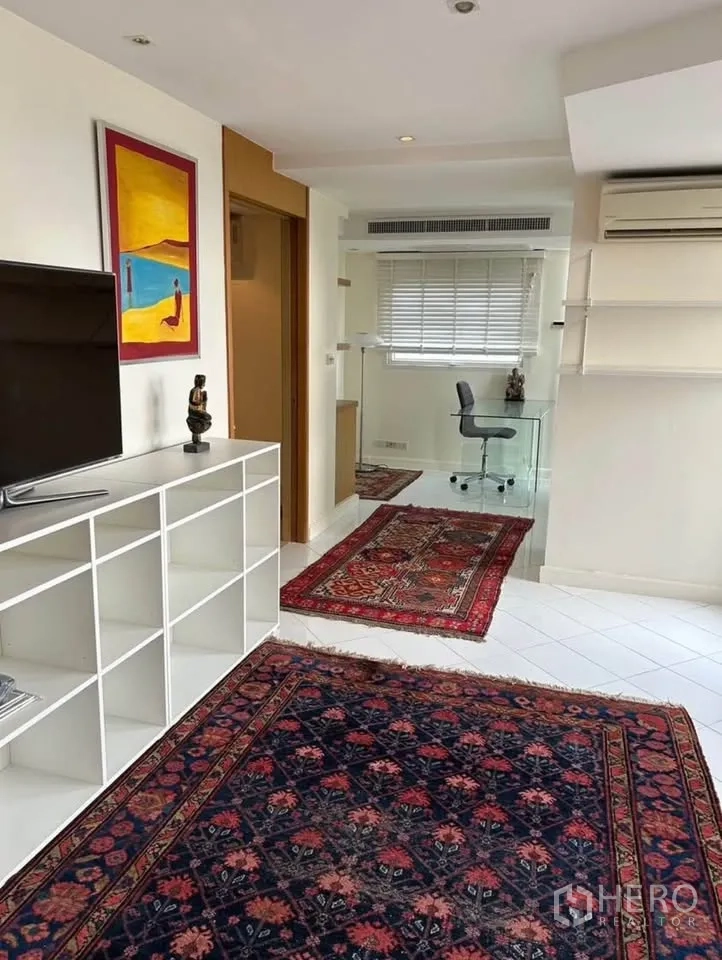 Condominium for rent or sale in Yan Nawa, Bangkok - Living zone with TV shelf wall, colorful artwork and glass study desk near balcony.