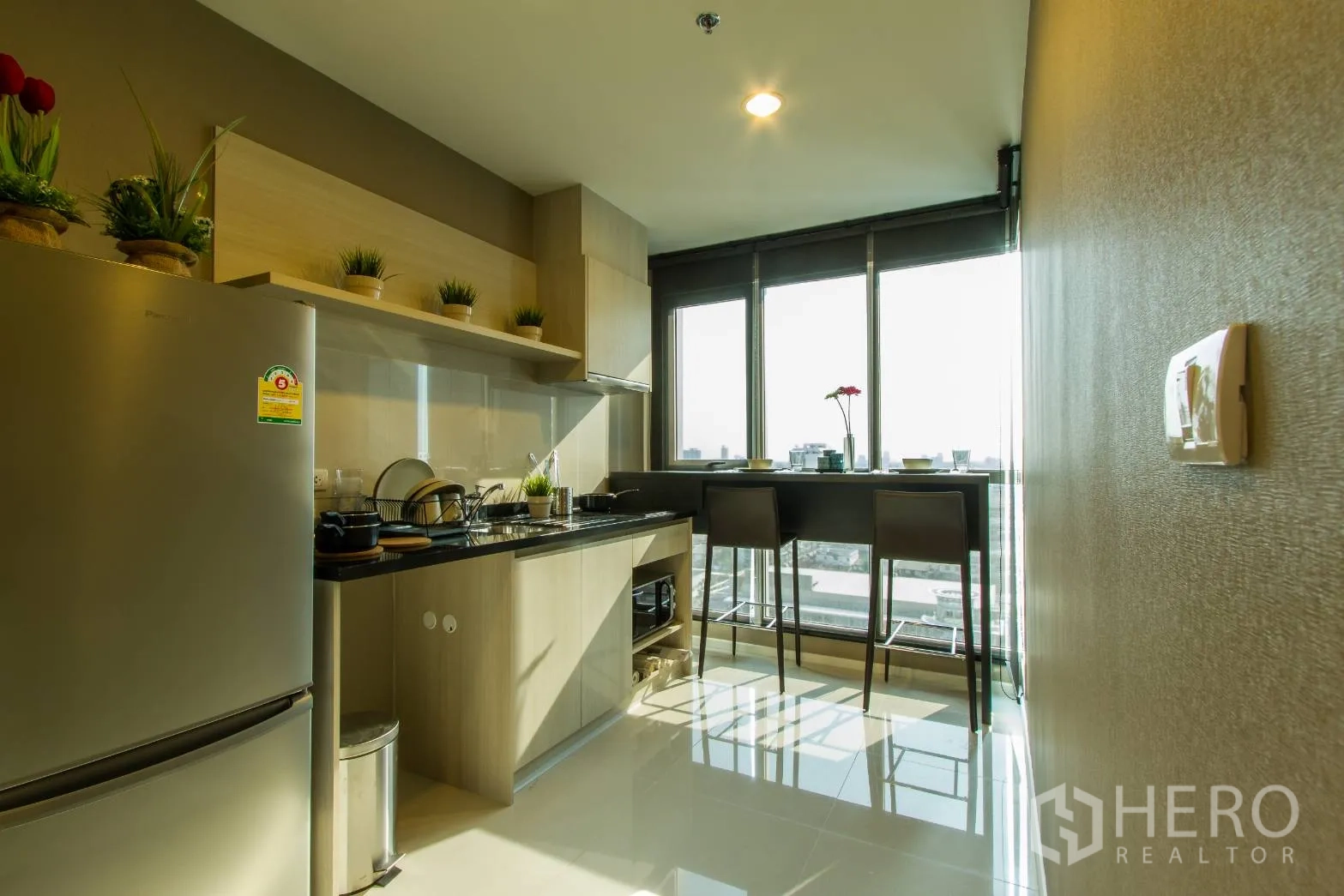 公寓 出租或出售在Sathon, Bangkok - 现代厨房，浅木柜体、黑色台面、不锈钢冰箱，窗边城市景观吧台。
