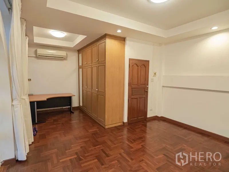 Townhouse for rent in Khlong Toei, Bangkok - Bright bedroom with large built‑in wooden wardrobe and recessed ceiling lights.