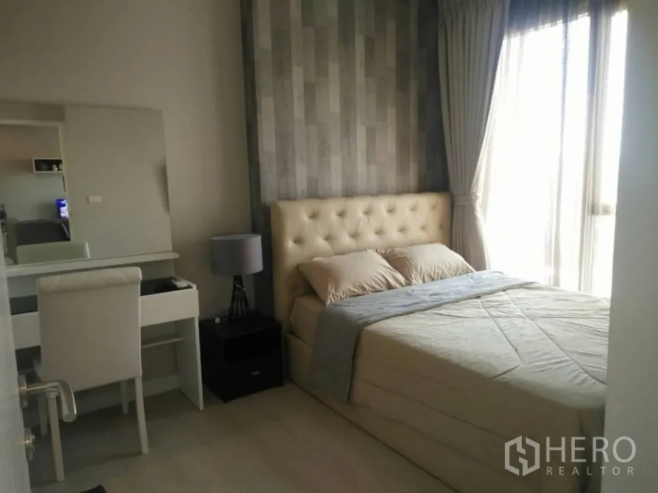 Condominium for rent or sale in Huai Khwang, Bangkok - Third bedroom with tufted headboard, study desk and large curtained window.