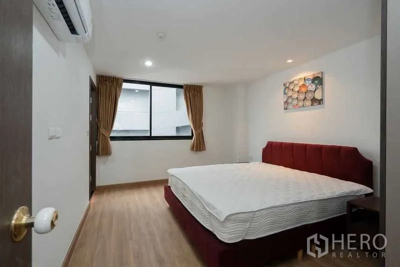 Apartment for rent in Khlong Toei, Bangkok - Master bedroom with red upholstered bed, window, wood floors and air conditioning.
