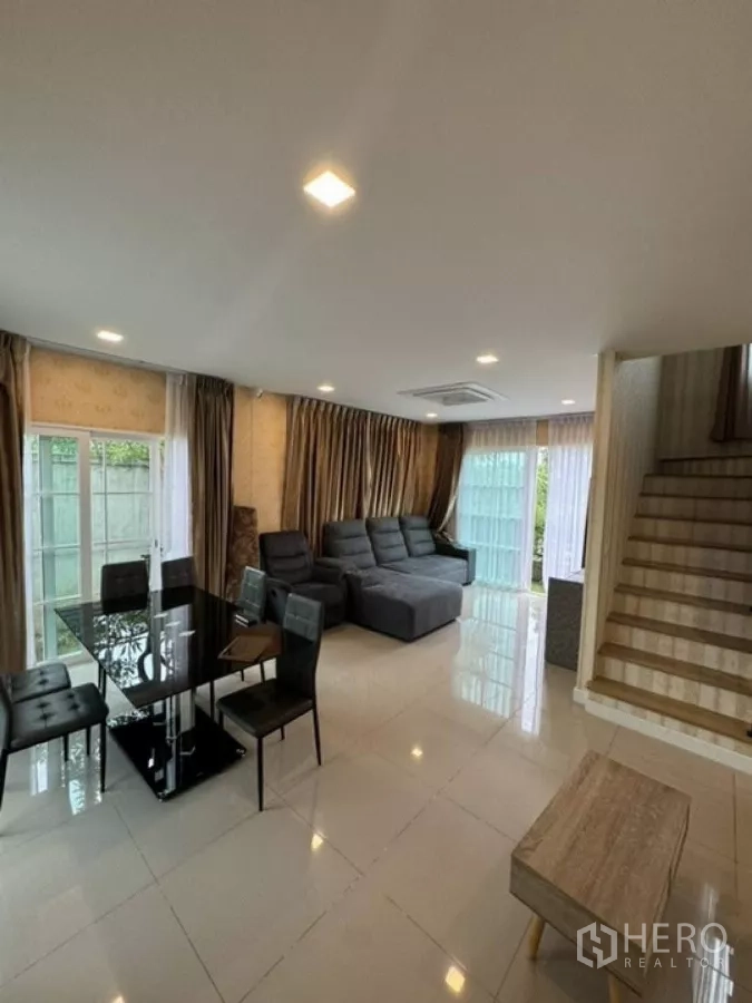Detached House for rent in Thanyaburi, Pathum Thani - Open-plan living and dining area with sectional sofa, glass table and staircase.