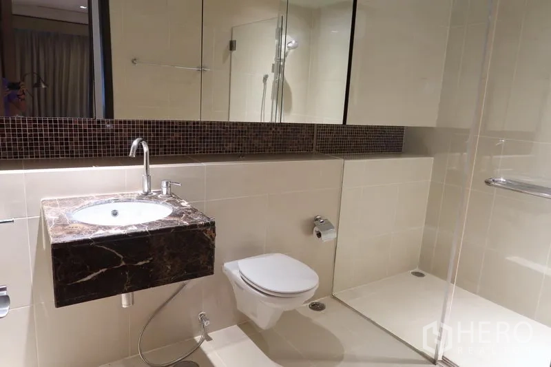 คอนโด ให้เช่าในKhlong Toei, Bangkok - ห้องน้ำที่สอง พร้อมฝักบัวกั้นกระจก โถสุขภัณฑ์แขวนผนัง และเคาน์เตอร์อ่างล้างหน้าหินอ่อน