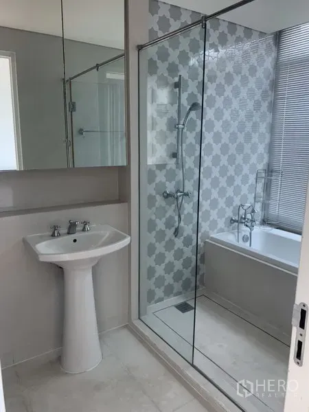 Condominium for rent or sale in Khlong Toei, Bangkok - Contemporary bathroom featuring a glass-enclosed shower, separate bathtub and pedestal sink with mirrored cabinet.