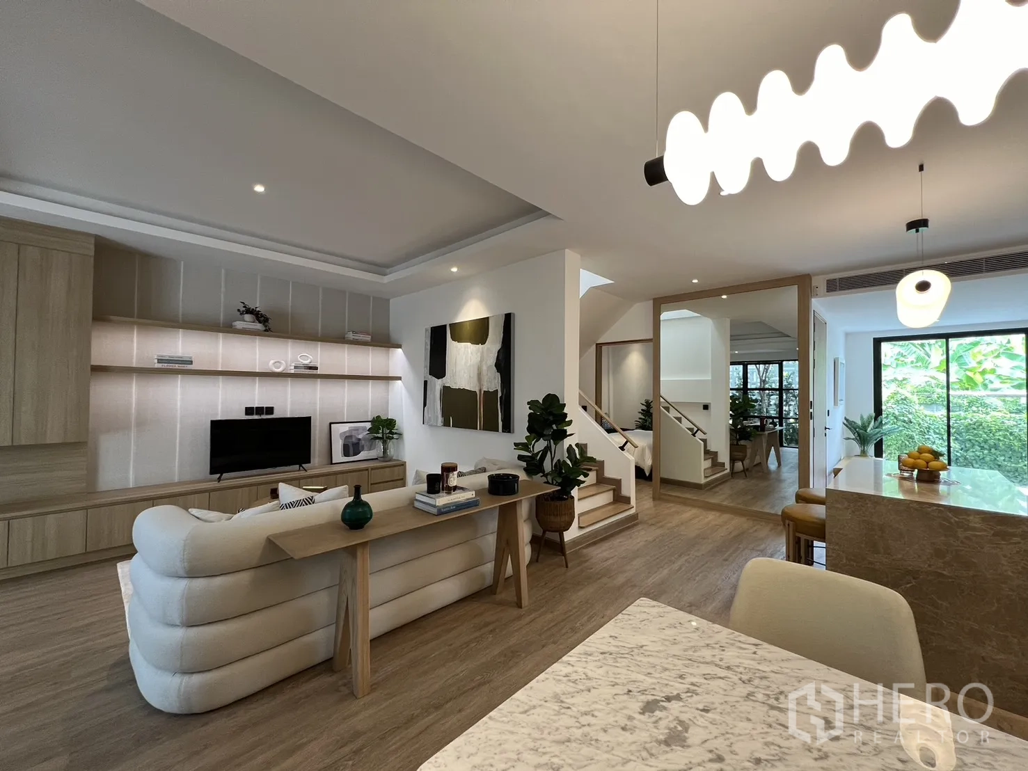 Townhouse for sale in Watthana, Bangkok - Open-plan living, dining and kitchen with wood flooring, sofa and modern lighting.