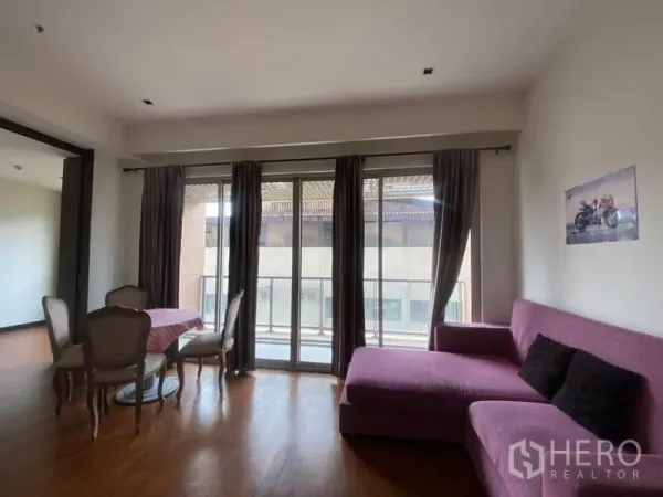 Condominium for rent in Yan Nawa, Bangkok - Living room with large sliding glass doors to the balcony, curtains, and an L-shaped purple sofa.