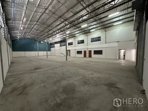 Warehouse for rent in Suan Luang, Bangkok - Open-plan warehouse bay with tall ceilings, skylights, steel columns, and white office partition walls along one side.