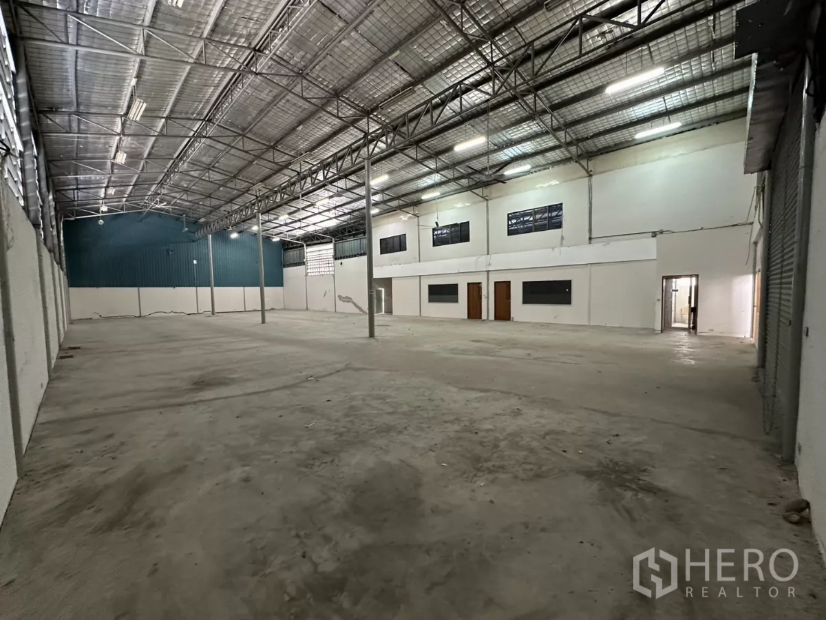 Warehouse for rent in Suan Luang, Bangkok - Open-plan warehouse bay with tall ceilings, skylights, steel columns, and white office partition walls along one side.