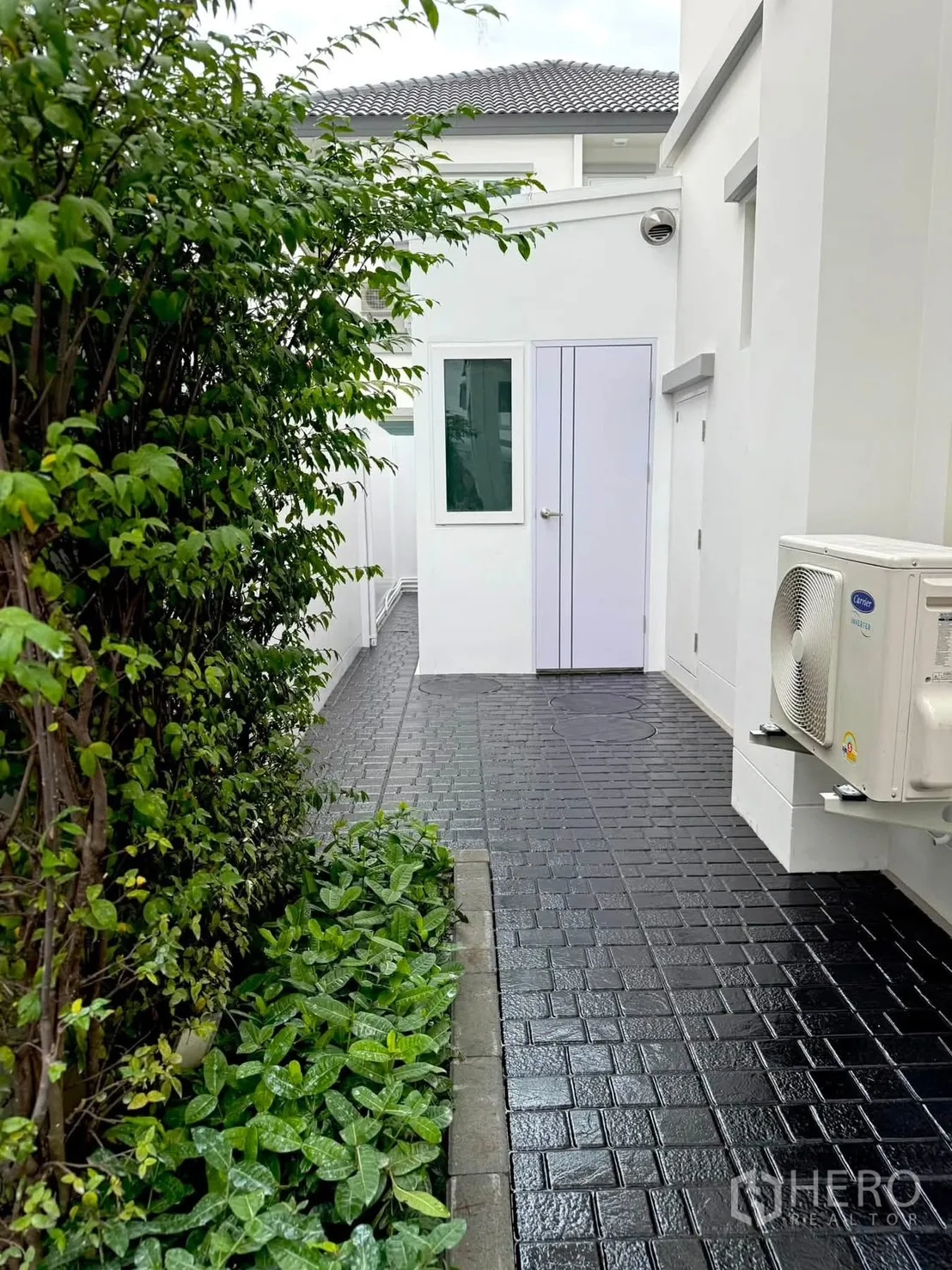 独栋房屋 for rent in Bang Phli, Samut Prakan - 房屋侧边铺装步道，绿篱与地被植物，白墙上挂外机。