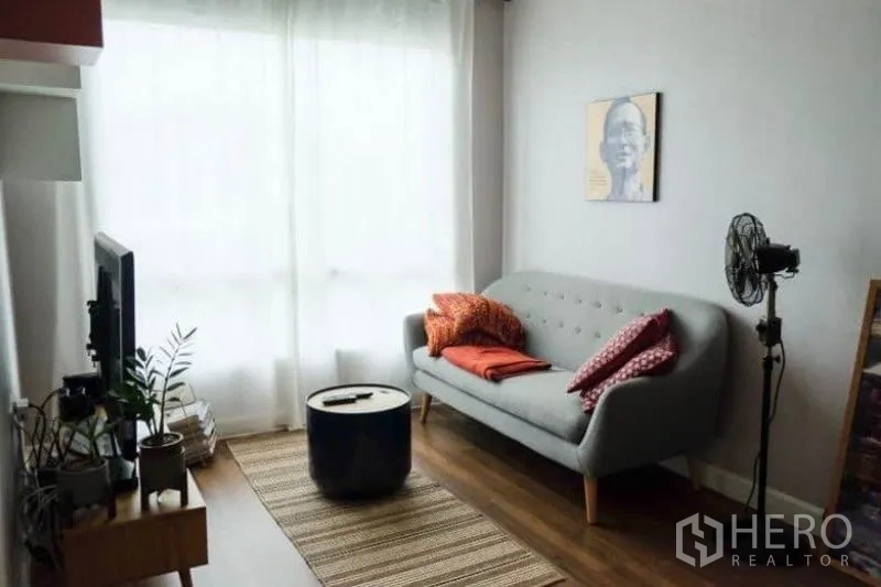 Detached House for rent or sale in Khlong Sam Wa, Bangkok - Cozy family room with grey sofa, TV stand, wood flooring and soft natural light.