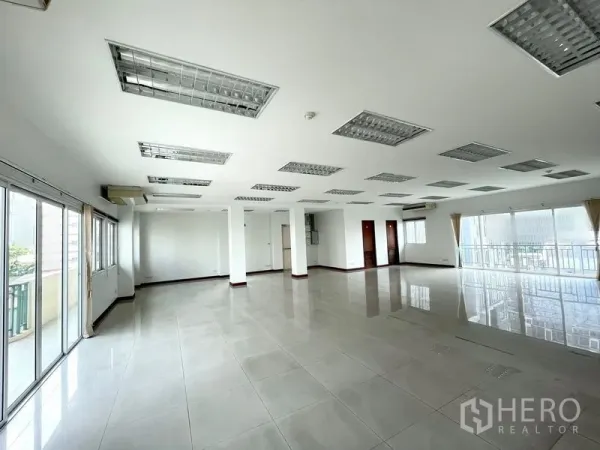 办公空间 出租在Bang Rak, Bangkok - 宽敞的开放式办公楼层，瓷砖地面、立柱、格栅吊顶灯与临阳台窗面。