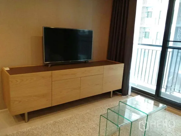 คอนโด ให้เช่าในKhlong Toei, Bangkok - มุมนั่งเล่นมีชั้นวางทีวีไม้ โต๊ะกระจกซ้อน และประตูกระจกบานเลื่อนออกสู่ระเบียง