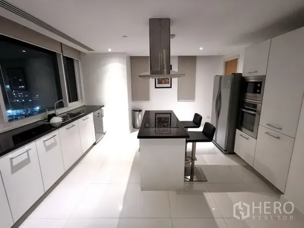 Condominium for rent in Watthana, Bangkok - Modern white kitchen with island cooktop, stainless appliances, and bar seating.