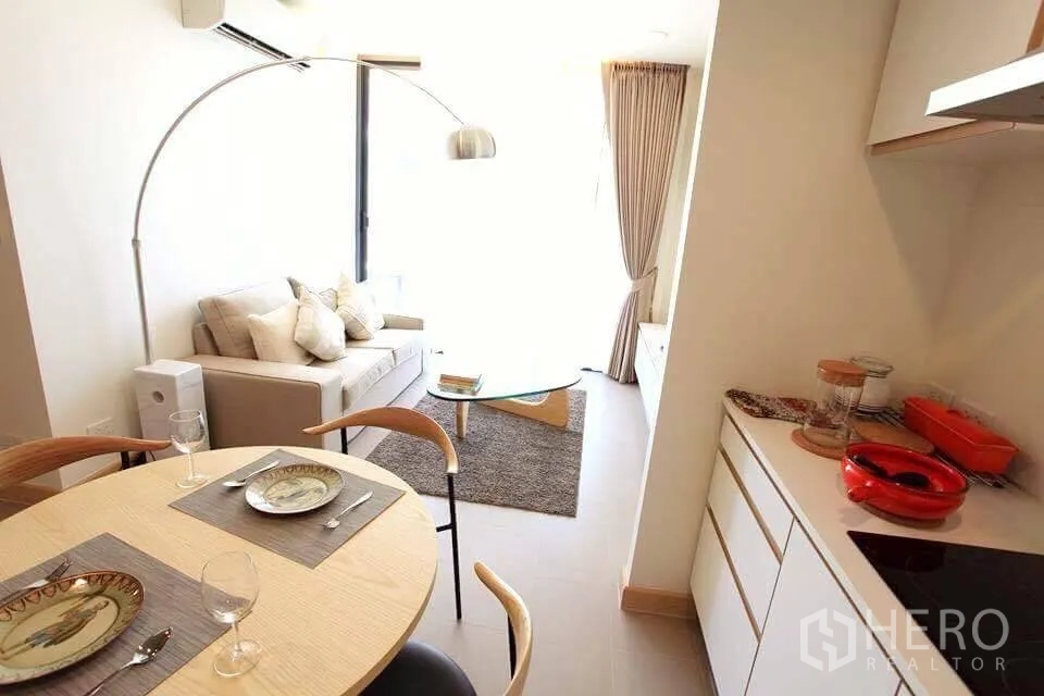 公寓 出租在Watthana, Bangkok - 餐区与紧凑厨房相连，延伸至采光充足的客厅，配弧形落地灯。