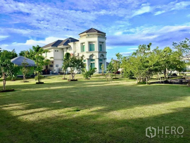 บ้าน ขายในKhlong Luang, Pathum Thani - สนามหญ้ากว้างมากพร้อมต้นไม้ นำสายตาไปยังบ้านสองชั้นสีขาวและอาคารประกอบ