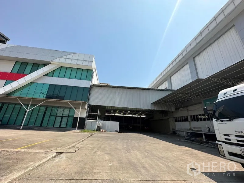 Warehouse for rent in Lam Luk Ka, Pathum Thani - Entrance court showing a glass-front office and canopied docks of the industrial complex.
