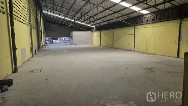 Warehouse for rent in Khlong Sam Wa, Bangkok - Open warehouse bay with high truss ceiling, yellow block walls and a roller shutter.