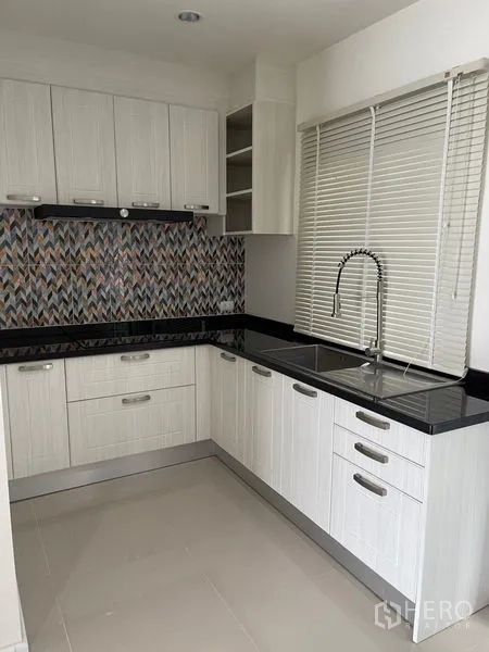 Townhouse for rent in Bang Kapi, Bangkok - Modern L-shaped kitchen with white cabinetry, black countertops and patterned backsplash.