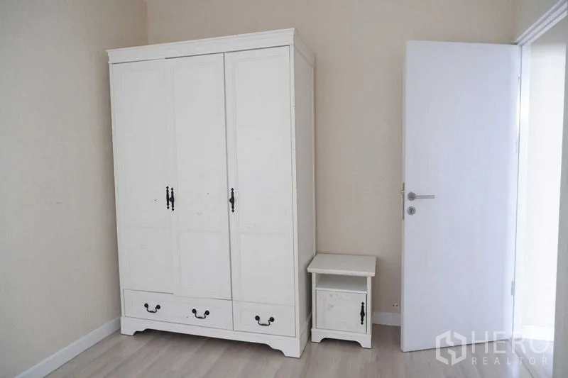 บ้าน ขายในLat Krabang, Bangkok - มุมห้องนอนเรียบง่ายพร้อมตู้เสื้อผ้าสีขาวและโต๊ะข้าง