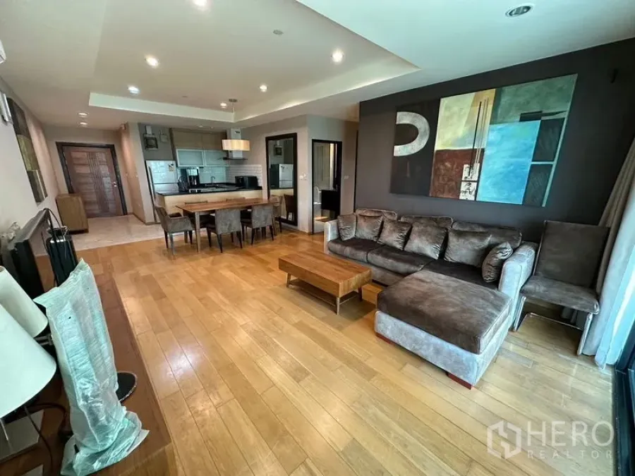 公寓 出租在Sathon, Bangkok - 沙吞公寓客厅，木地板、L型沙发、餐桌与大幅装饰画