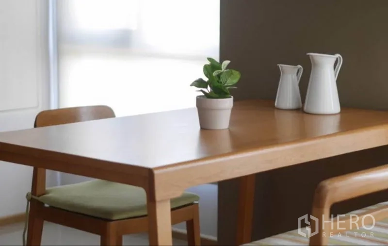 คอนโด ให้เช่าในPhaya Thai, Bangkok - ภาพระยะใกล้โต๊ะอาหารไม้ พร้อมกระถางต้นไม้และเหยือกตกแต่งข้างหน้าต่างแสงนุ่ม