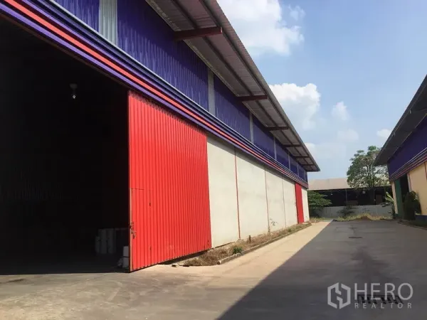 Warehouse for rent in Sai Noi, Nonthaburi - Colorful warehouse exterior with a large red sliding door and covered loading eave.