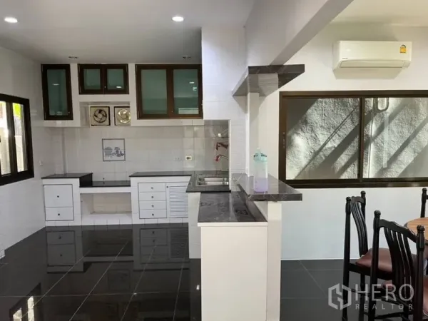 独立式住宅 出租在Samut Prakan - 开放式厨房，黑色花岗岩台面、白色橱柜与大窗户。