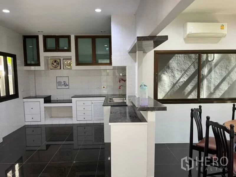 独立式住宅 出租在Samut Prakan - 开放式厨房，黑色花岗岩台面、白色橱柜与大窗户。